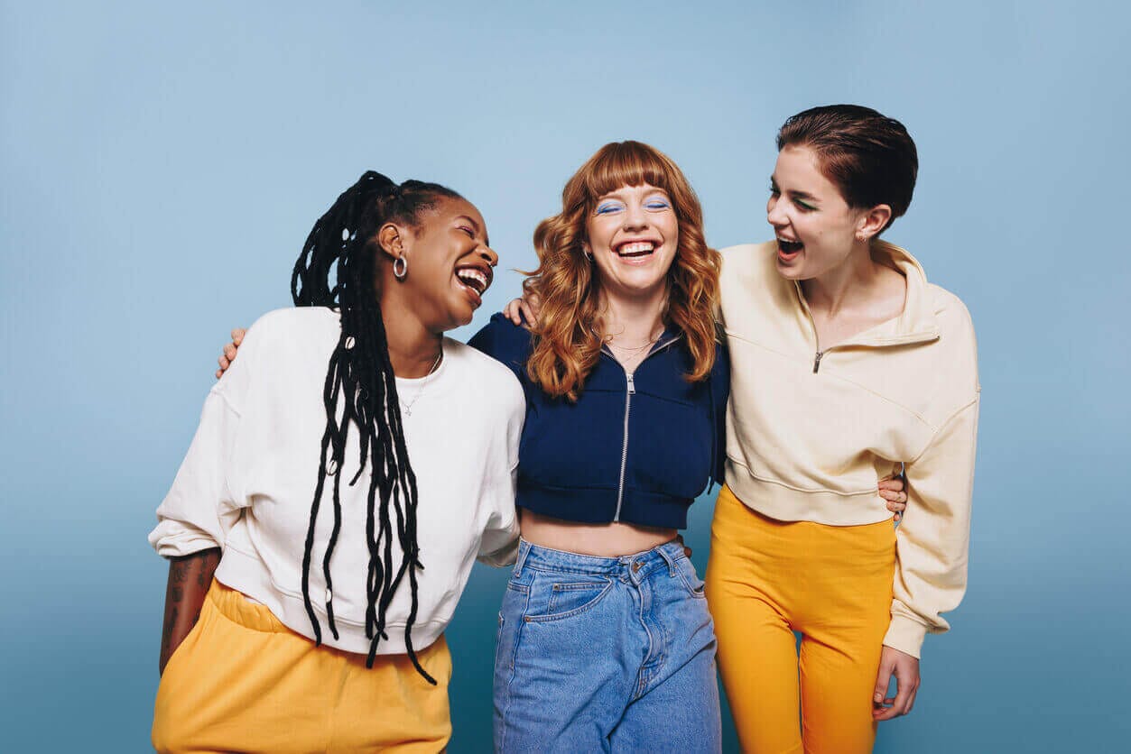 Three teenage girls laughing and embracing each other against a blue background.