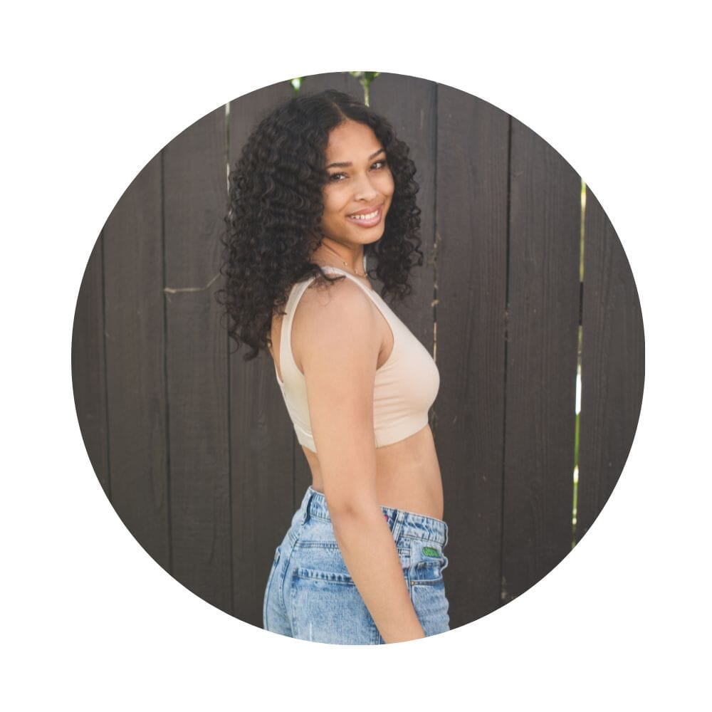 Sand-Rose# A young woman with blonde hair smiling and looking over her shoulder, wearing an Sand-Rosecolor aster organic tank bra.