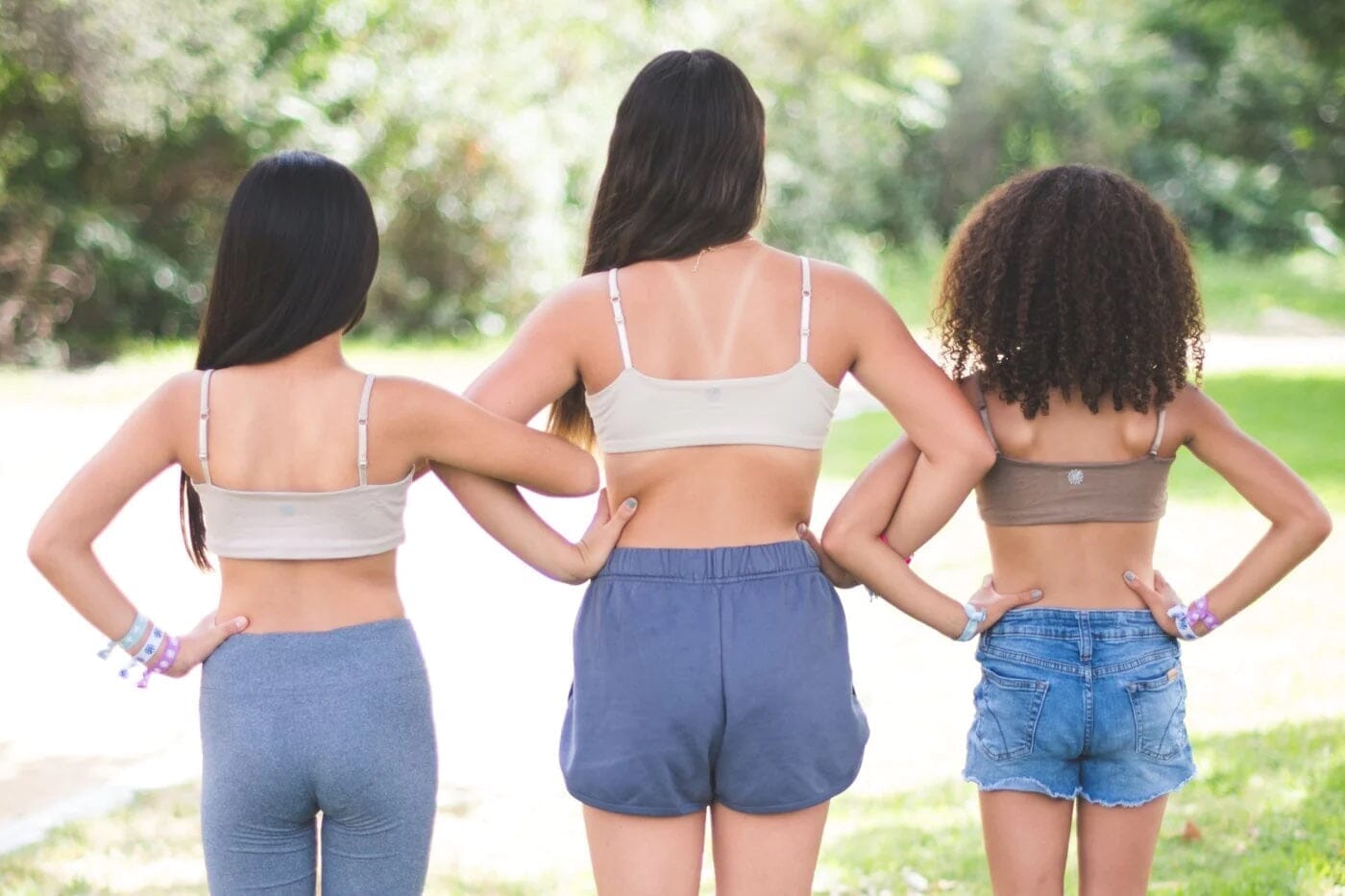 Three girls standing side by side with their hands on their hips, showcasing different styles and fits of training bras, highlighting comfort and support for various body types.