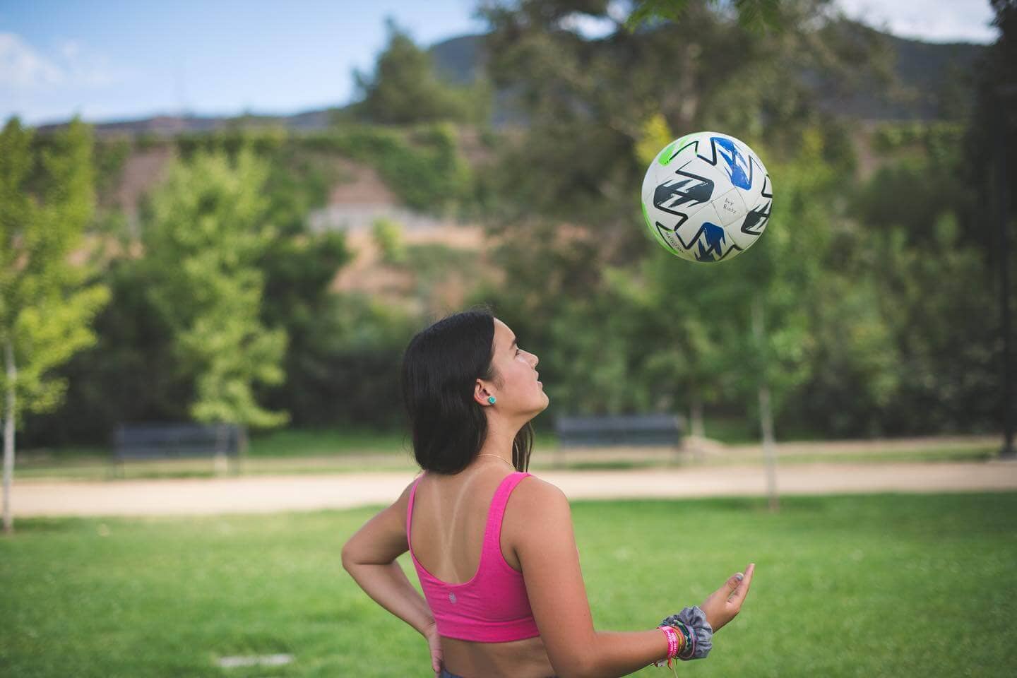 A teen girl wearing a Bleuet bra throws a soccer ball in the air in a park. 