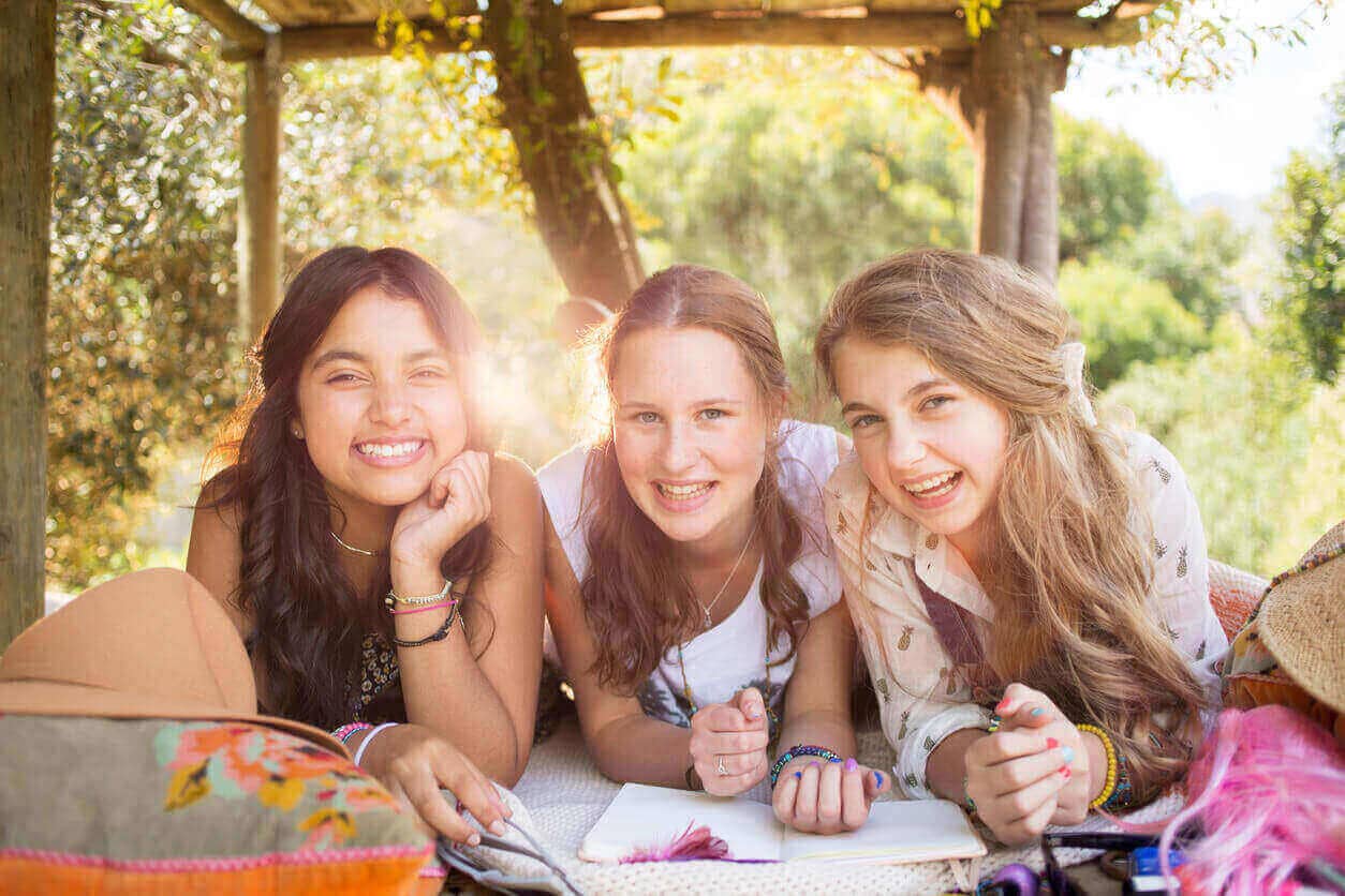 Three happy and smiling teenage girls lying outdoors together on a sunny day.