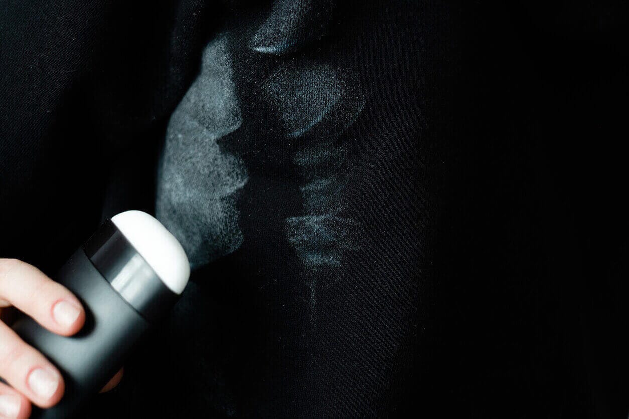 Close-up of a hand applying deodorant, leaving visible white stains on a black fabric.