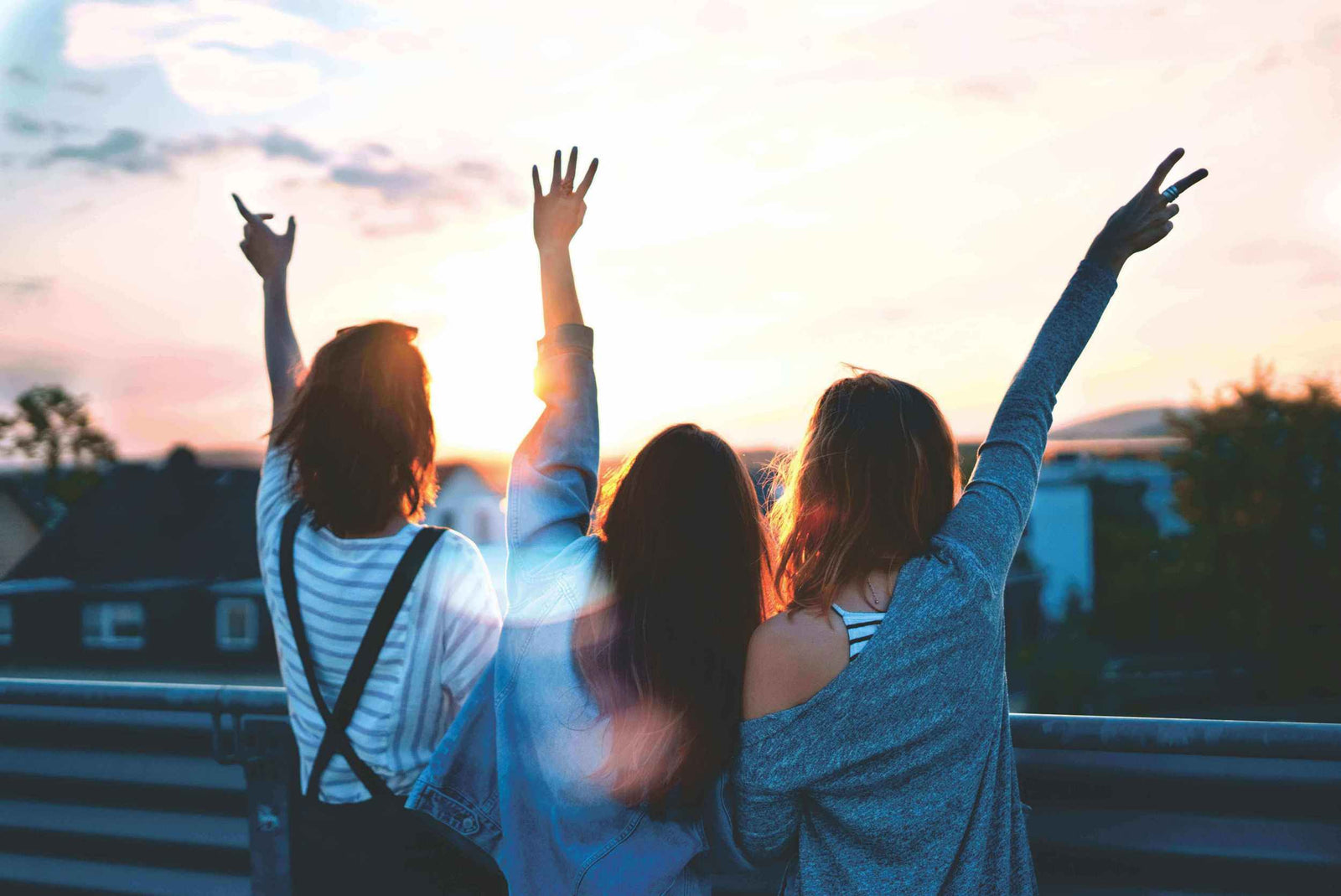 Three teens standing on a rooftop at sunset, raising their hands, with a warm glow surrounding them.