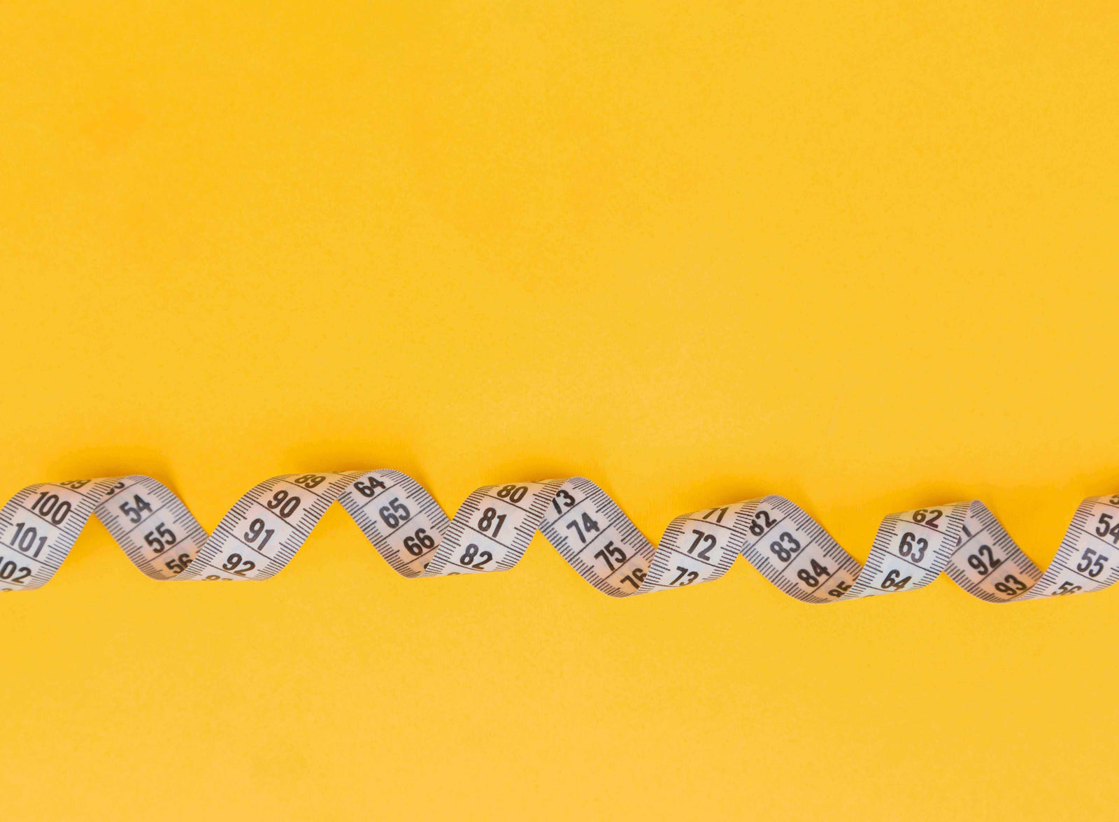A curled measuring tape with black numbers against a bright yellow background.