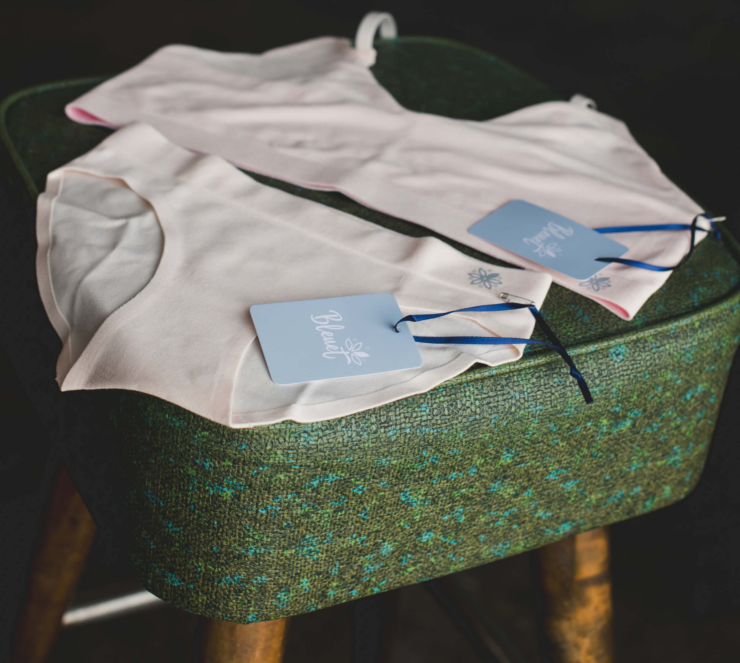 Photo of nude-colored underwear from Bleuet laid out on a green chair, demonstrating that nude is a great solution to the question, “what color bra to wear under white?”