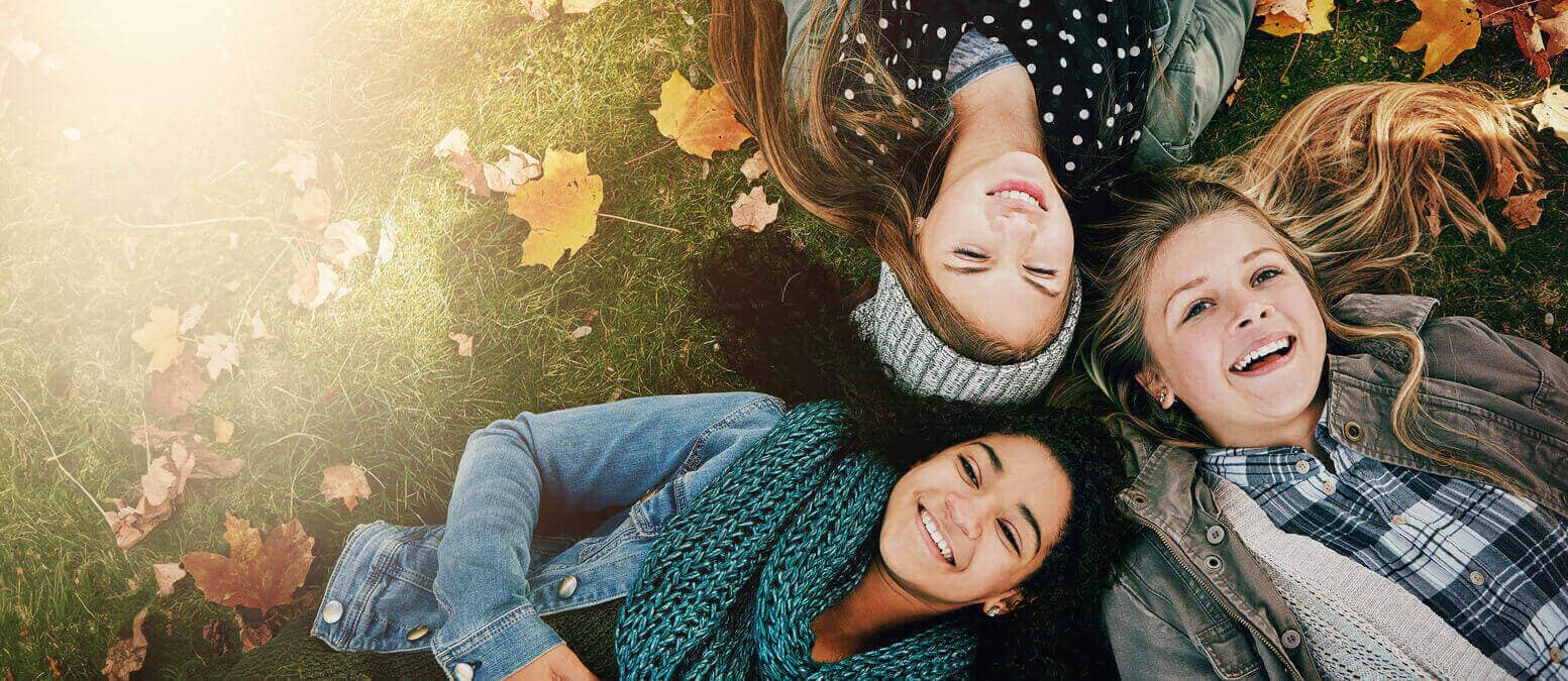 Three teenage girls lying on the grass and smiling.