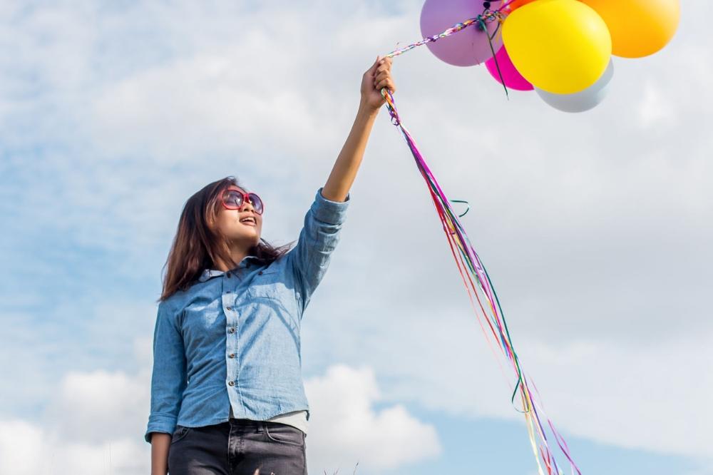 Tween girl confidently holding colorful balloons in a field