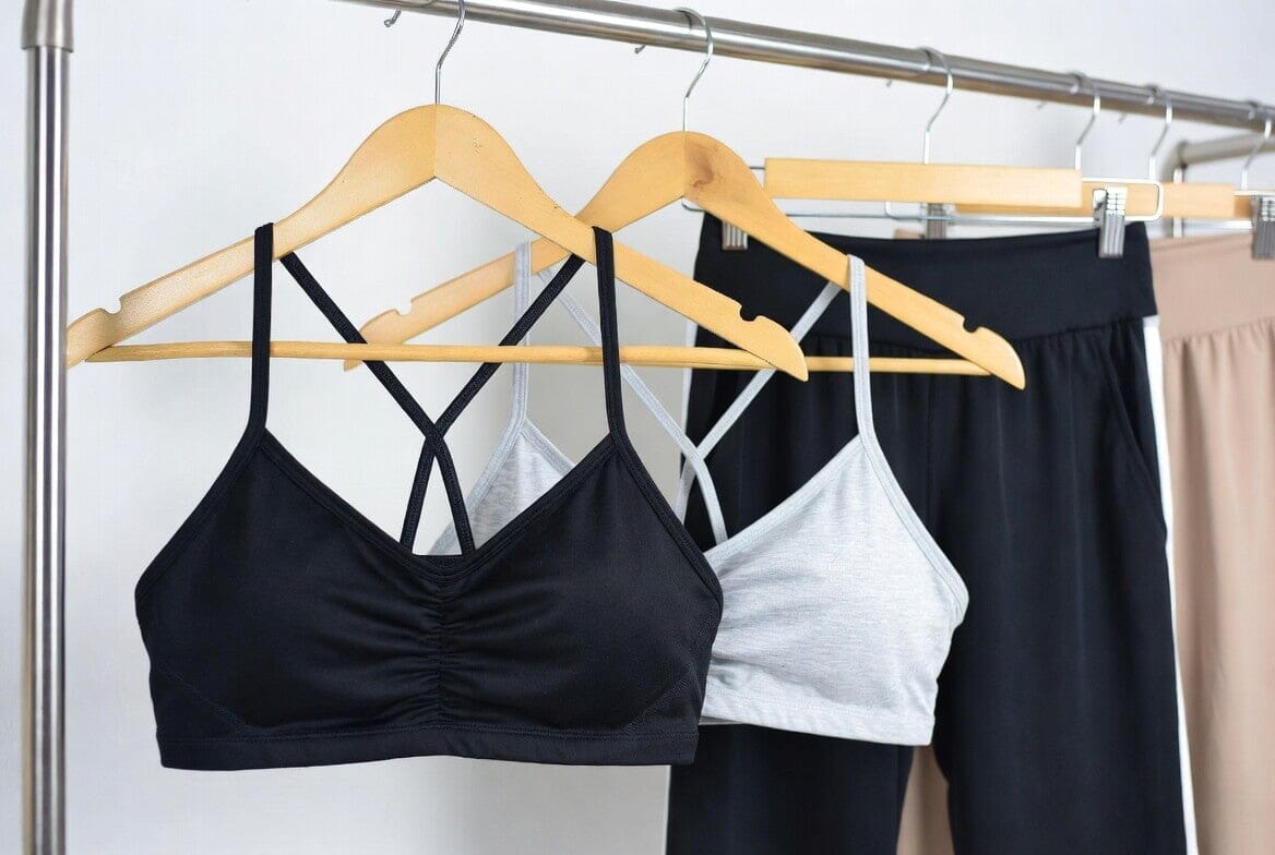 Several soft sports bras (black, grey, and others) with criss-cross back straps hanging on wooden hangers in a clothing store.