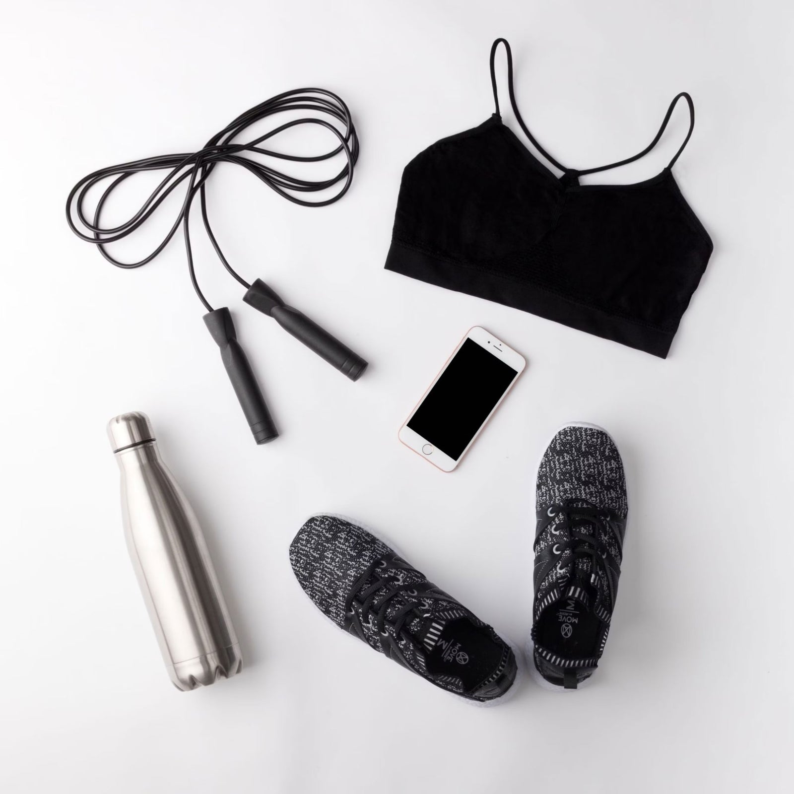 A black sports bra, black athletic shoes, a jump rope, a smartphone, and a stainless steel water bottle arranged on a white background.