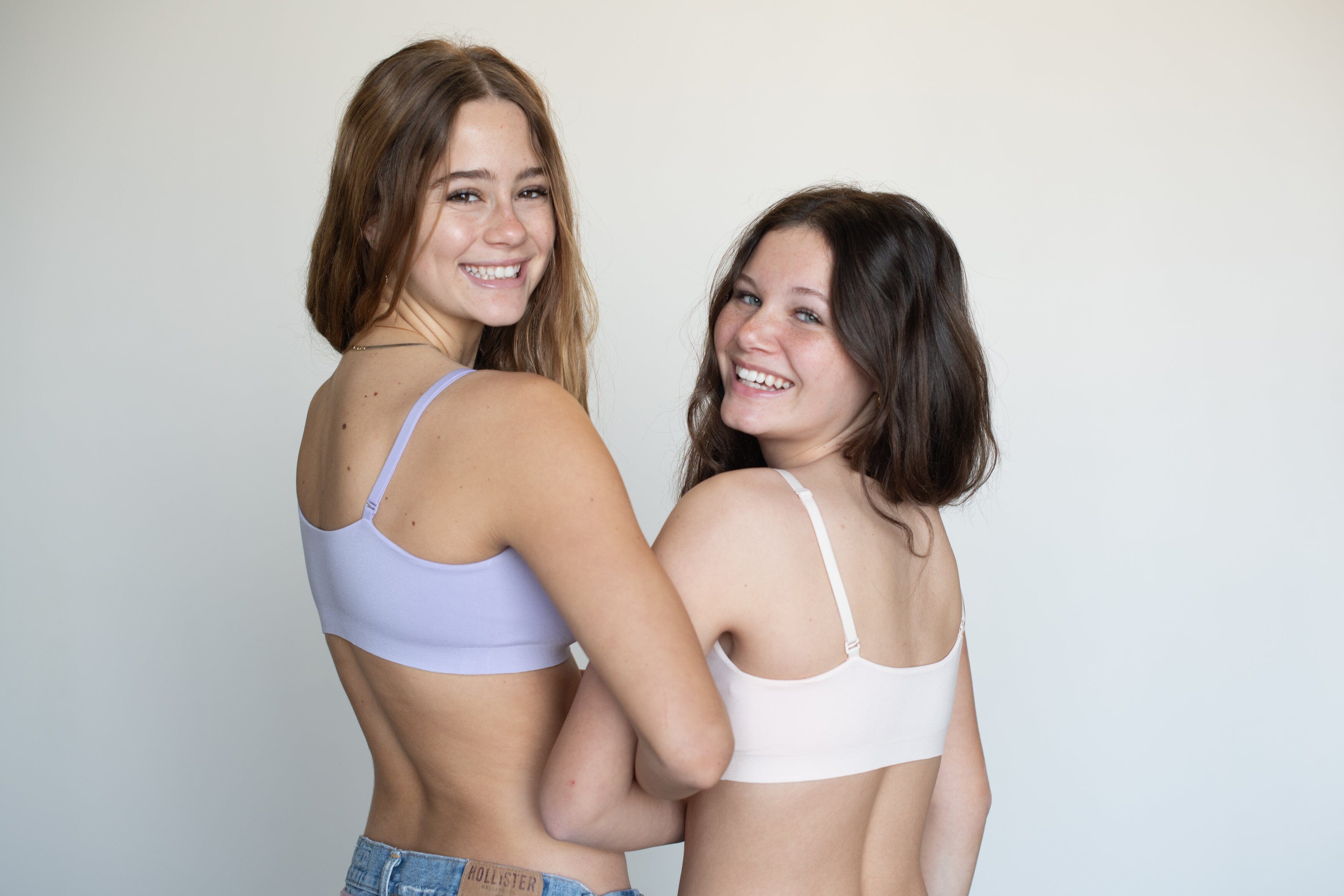 An image of two backfacing, smiling teenage girls in sports bras holding hands.