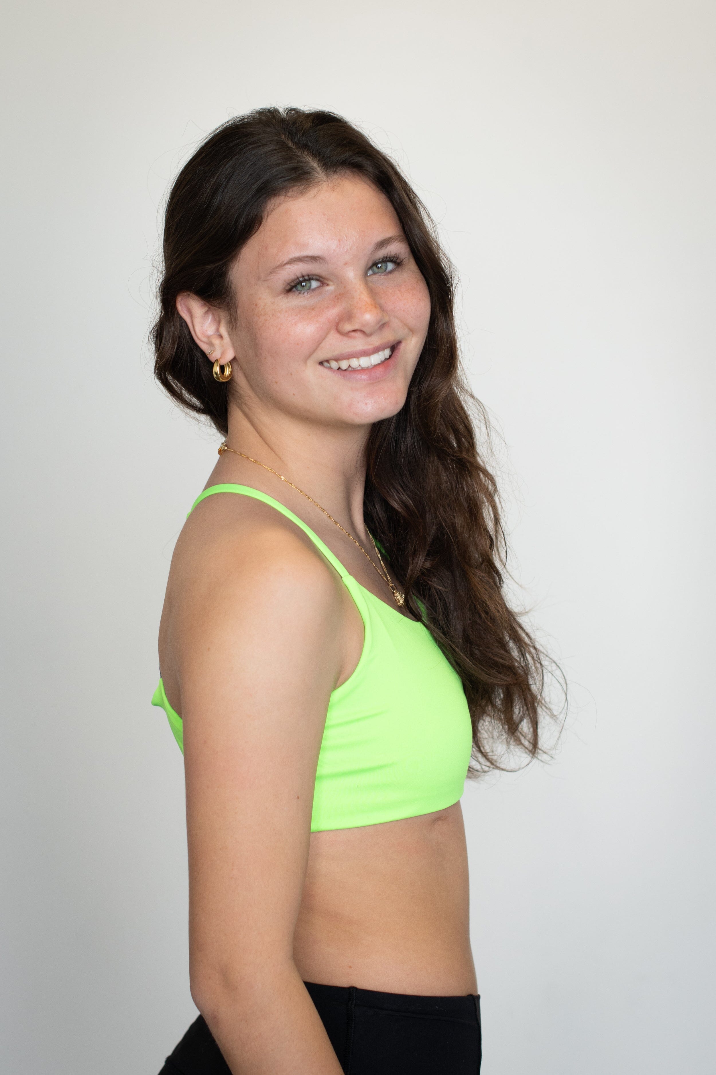 Teen girl in a bright neon green bralette by Bleuet smiles confidently in profile, showcasing a comfortable everyday bra for growing bodies.