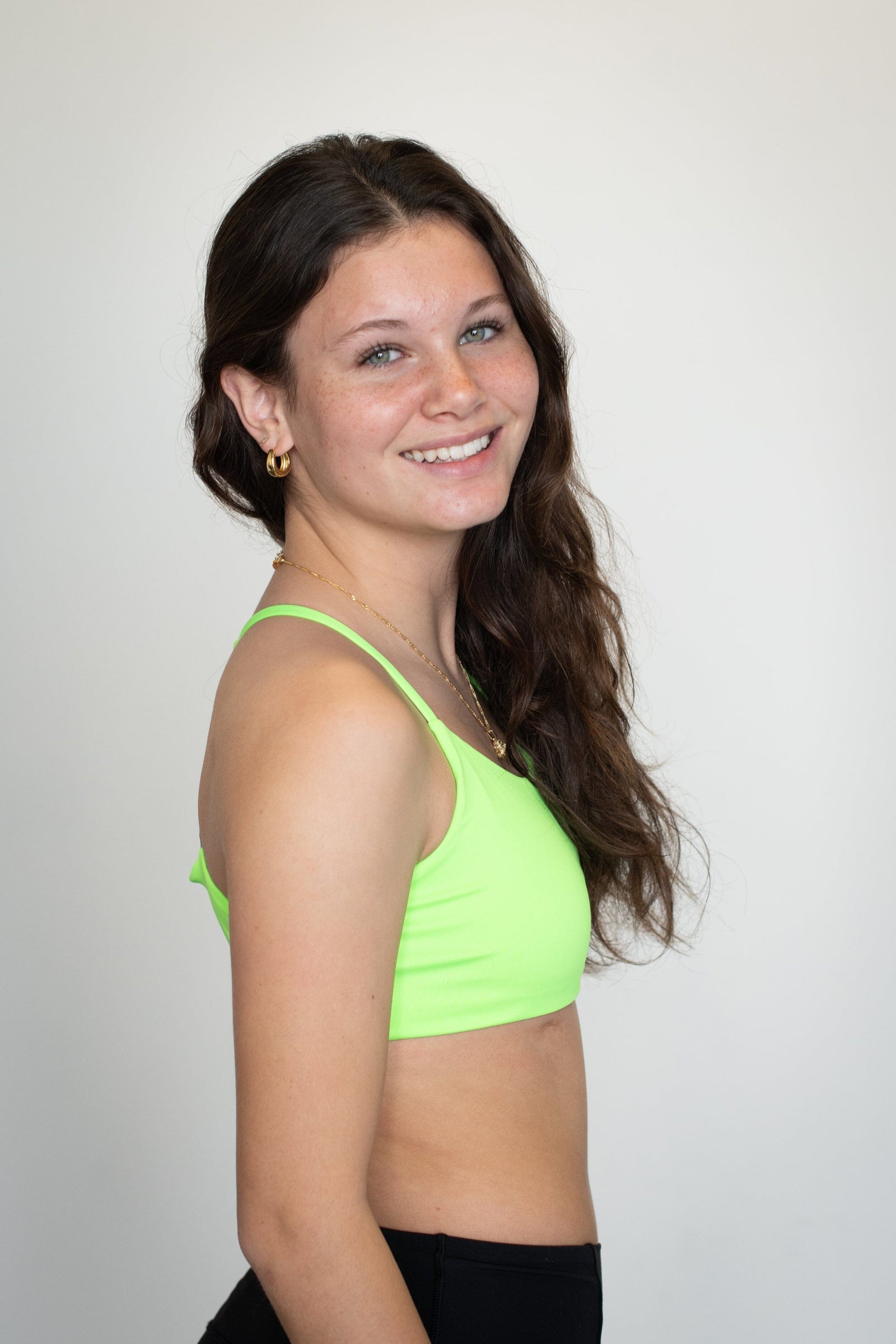 Teen girl in a bright neon green bralette by Bleuet smiles confidently in profile, showcasing a comfortable everyday bra for growing bodies.