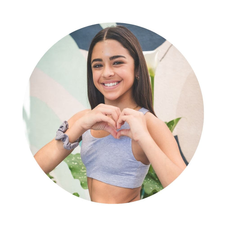 A young woman with curly hair smiling and looking over her shoulder, wearing a gray racerback bra