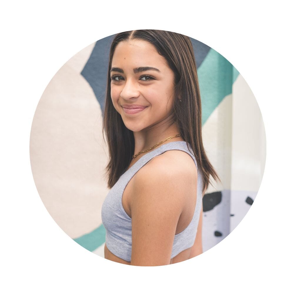 Grey-Lake#A young woman with curly hair smiling and looking over her shoulder, wearing a gray racerback bra