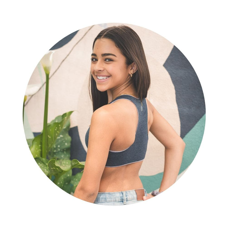 A young woman with curly hair smiling and looking over her shoulder, wearing a gray racerback bra