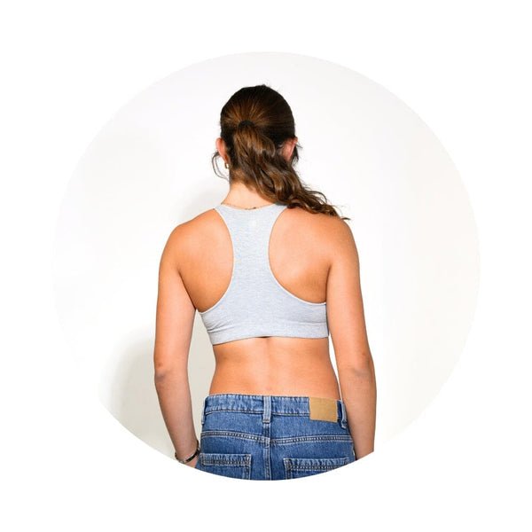 A woman viewed from behind wearing a light gray racerback sports bra and blue jeans, centered within a white circular frame on a white background.