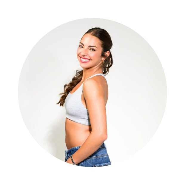 Grey-Lake#A smiling woman with dark hair tied back, wearing a light gray ribbed crop top and blue denim shorts, posed inside a circular frame against a plain white background.