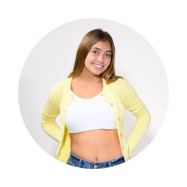 A smiling young woman with light brown hair is shown from the waist up, wearing a pale yellow cardigan over a white crop top and blue jeans, set against a light gray circular background on a white field.
