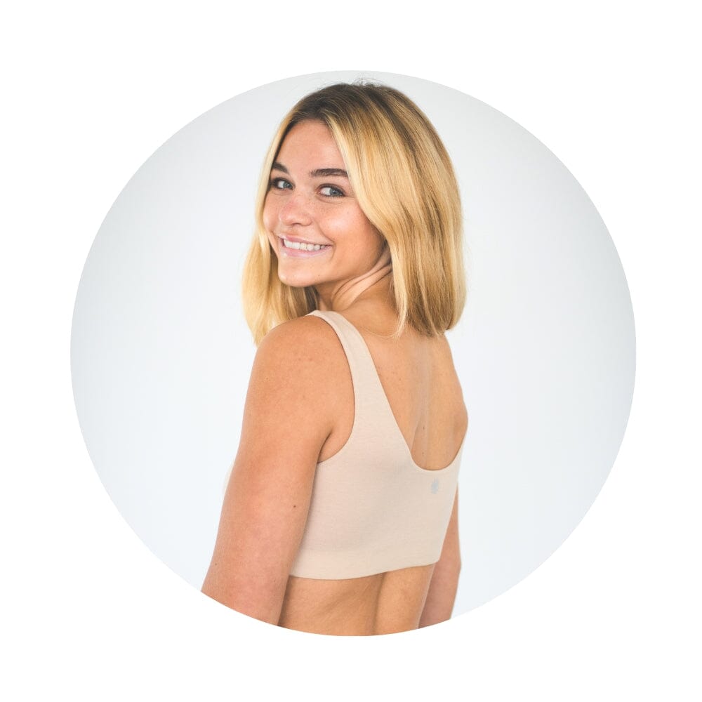 Sand-Rose# A young woman with blonde hair smiling and looking over her shoulder, wearing an Sand-Rosecolor aster organic tank bra. 