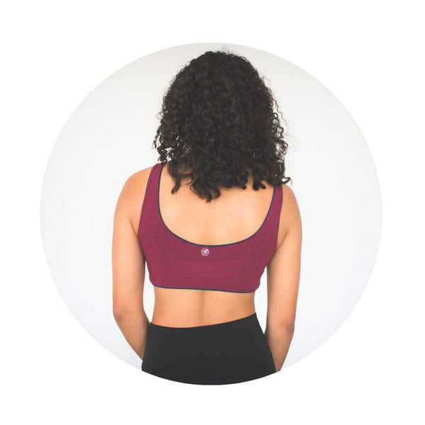 Back view of a model wearing a maroon Aster Organic Tank Bra with teal lining, showing the bra's design and logo.
