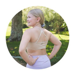 Tween girl in a beige sports bra and purple leggings standing outdoors with trees in the background
