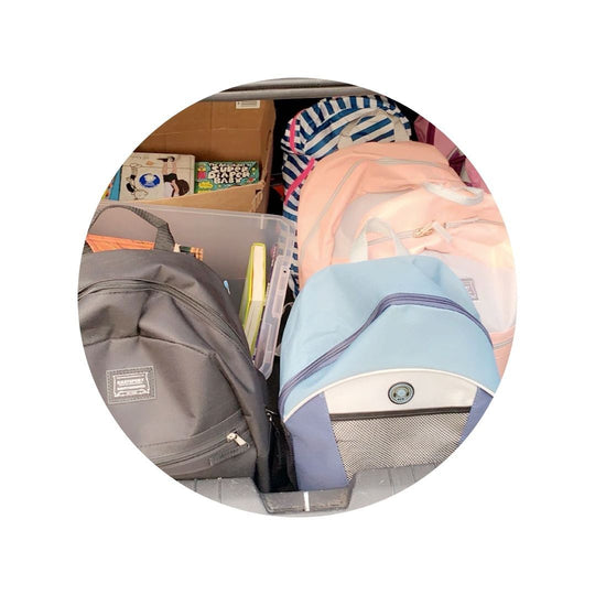 Gift#Backpack for Foster Teen#Various backpacks, including a black, blue, and pink one, packed inside a car trunk.