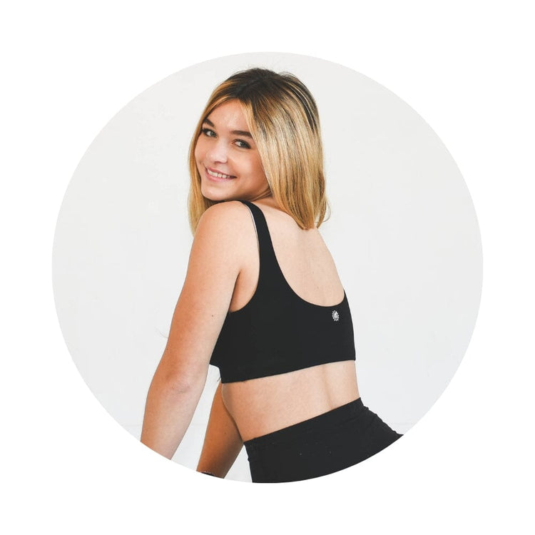 Black-Grey#A girl with long blonde hair wearing a black Aster Organic Tank Bra from Bleuet. She is facing backward and smiling over her shoulder. Black-Grey#Organic Bras & Bralettes For Girls, Tweens and Teens